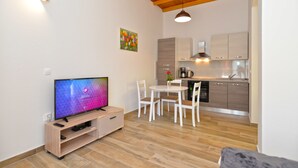 A modern living room with a flat-screen TV, a dining table with chairs, and a kitchen area with wooden cabinets and a sink. - Apartment 1674 (Pula)
