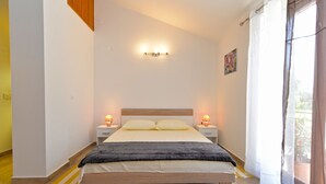 A bedroom with a wooden bed, two bedside tables with lamps, a painting on the wall, and a window with curtains. - Apartment 1674 (Pula)