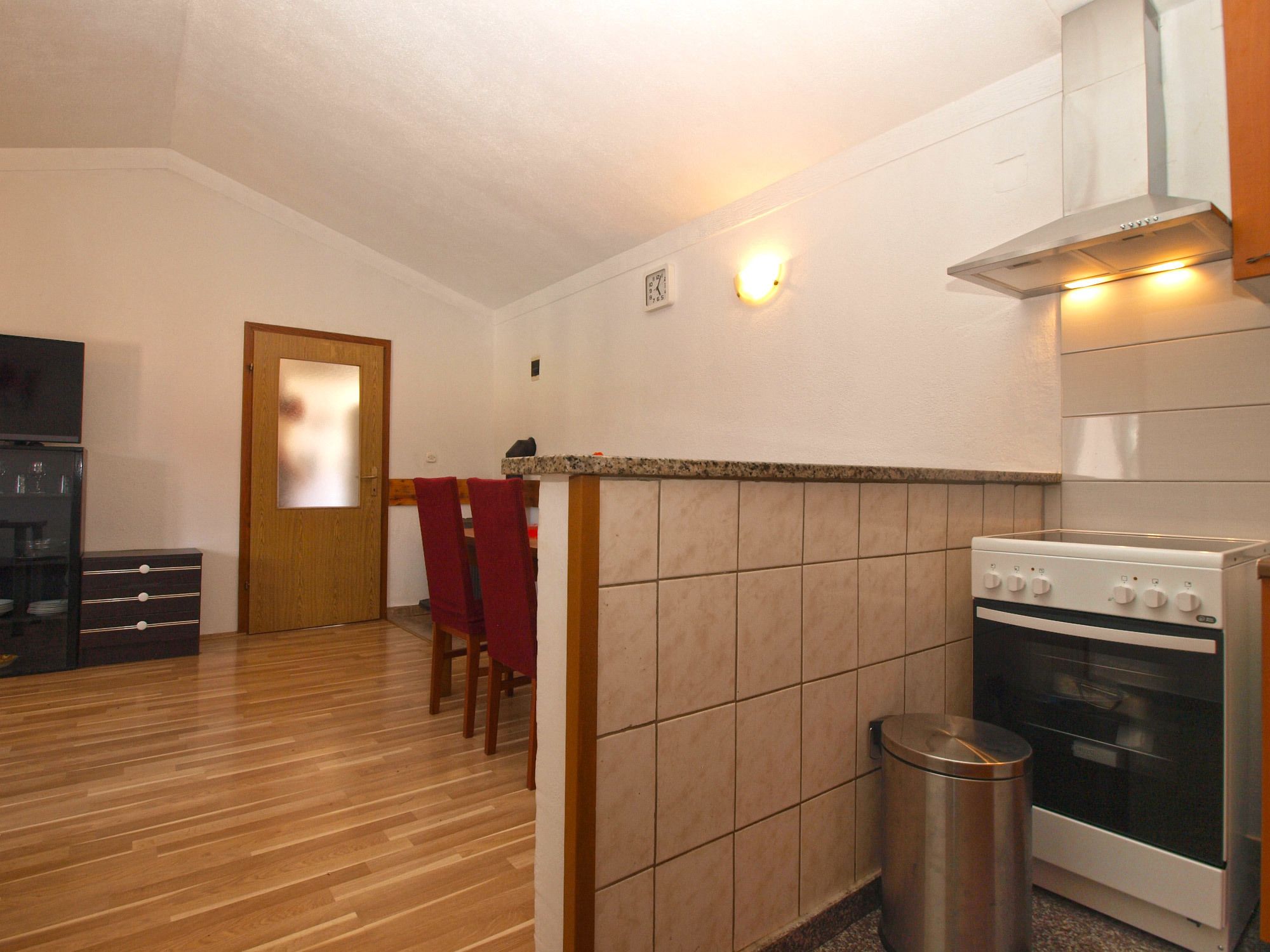 A compact kitchen with a stove, oven, and a small trash bin.