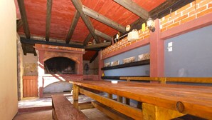 A rustic dining area with a brick fireplace, wooden benches, and a brick wall with shelves.