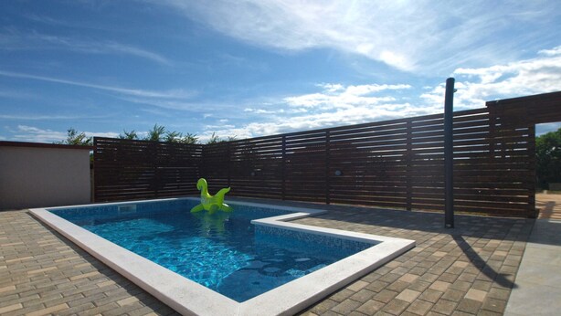 A rectangular swimming pool with a tiled edge, surrounded by a brick patio.