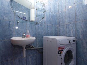 A bathroom with a sink, a glass shower enclosure, and a front-loading washing machine. - Apartment 1680 (Pula)