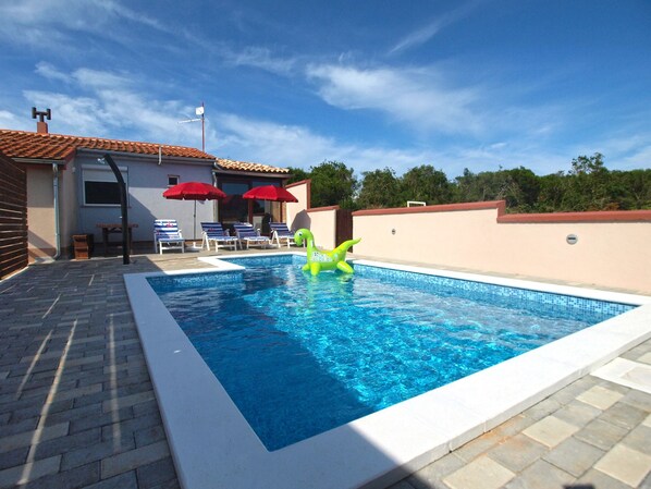 A swimming pool with a green inflatable toy, red umbrellas, and lounge chairs. - Apartment 1680 (Pula)