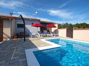 A swimming pool with lounge chairs and umbrellas, a tiled deck, and a building with a tiled roof. - Apartment 1680 (Pula)