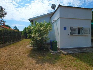 Simple, single-story building with a flat roof and a satellite dish, set amidst a lush lawn and surrounded by a metal fence.