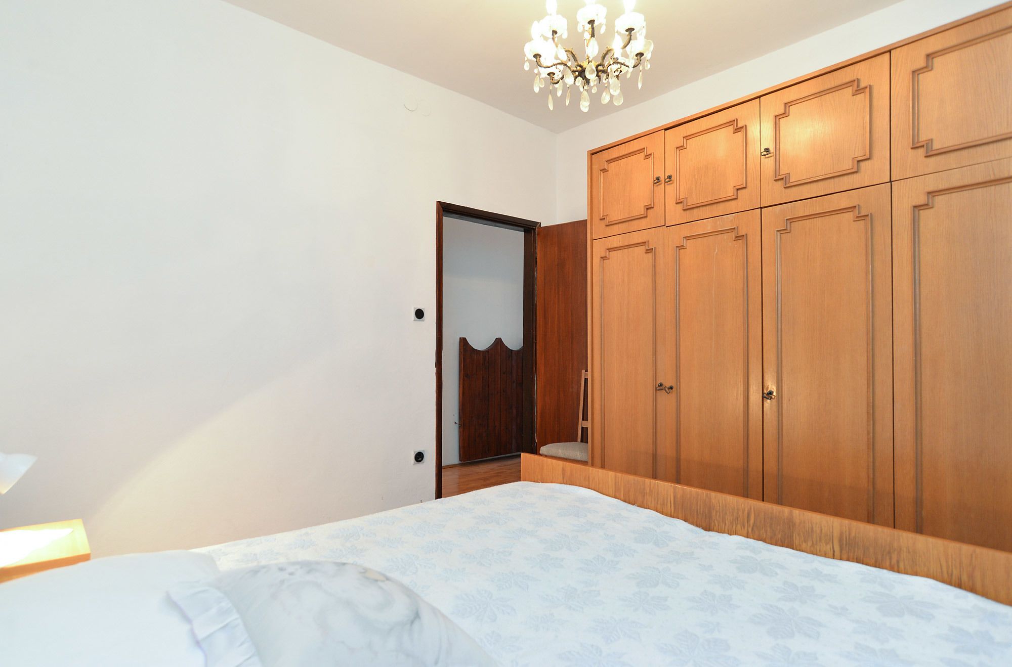 A bedroom with a bed, wooden wardrobe, and a chandelier.