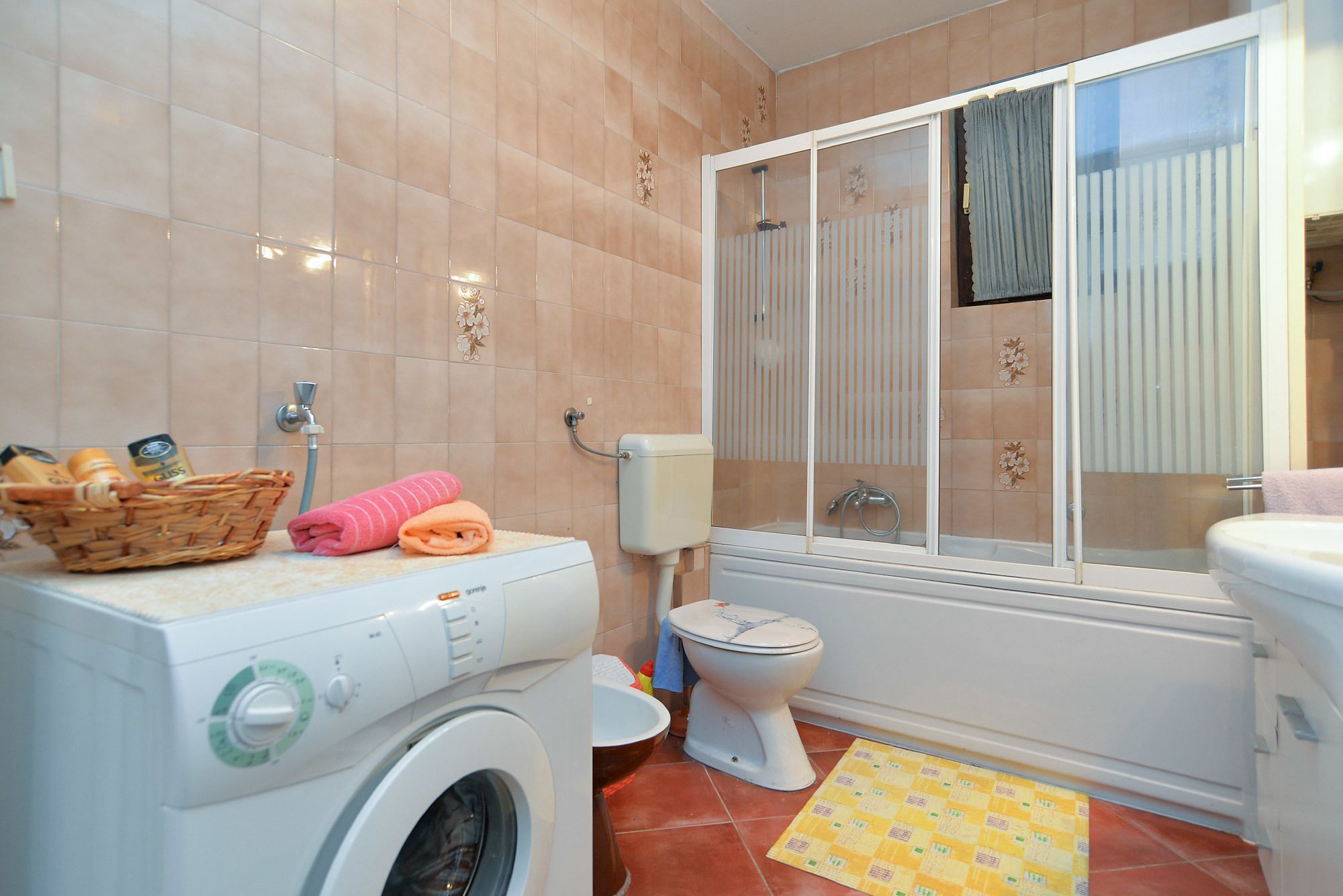 A bathroom with a washing machine, toilet, and a window with a curtain.