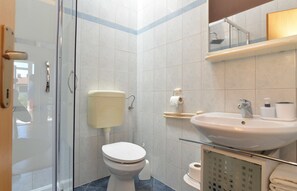 A modern bathroom with a toilet, sink, and glass shower enclosure. - Apartment 1692 (Fazana)