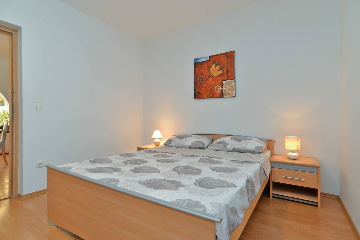 A bedroom with a bed, two bedside tables, a wall-mounted artwork, and a door leading to another room.