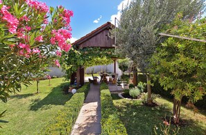 A garden with a wooden pergola, outdoor seating, and a pathway leading to a building with a sloped roof. - Apartment 1692 (Fazana)