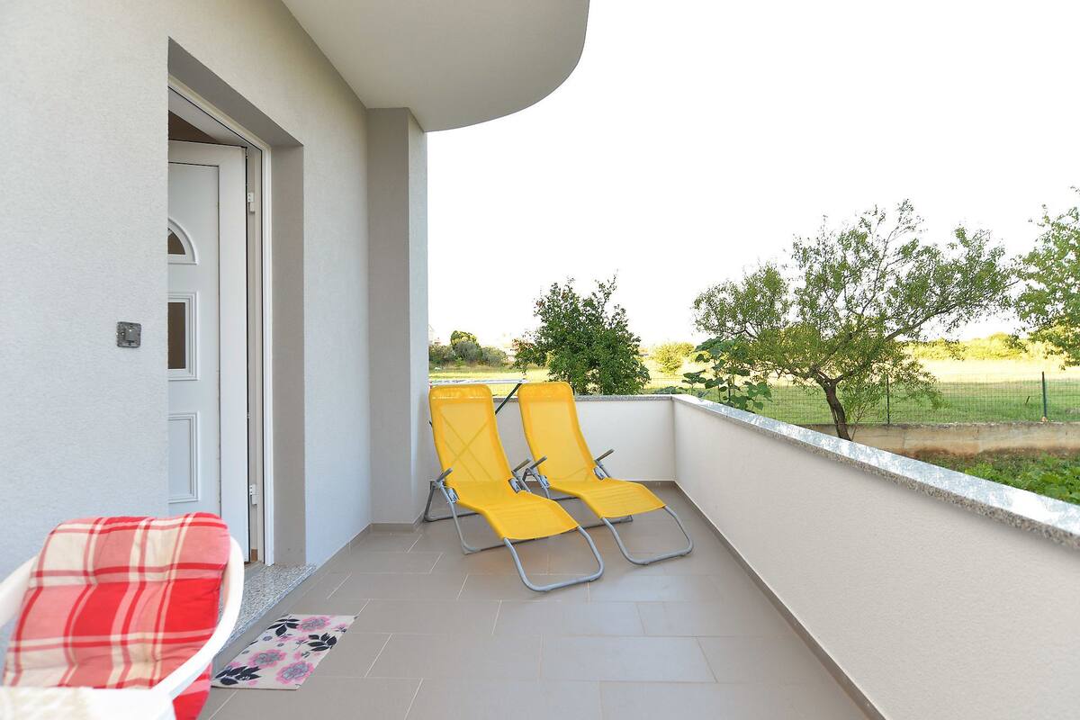A balcony with two yellow chairs, a red and white chair, and a door.