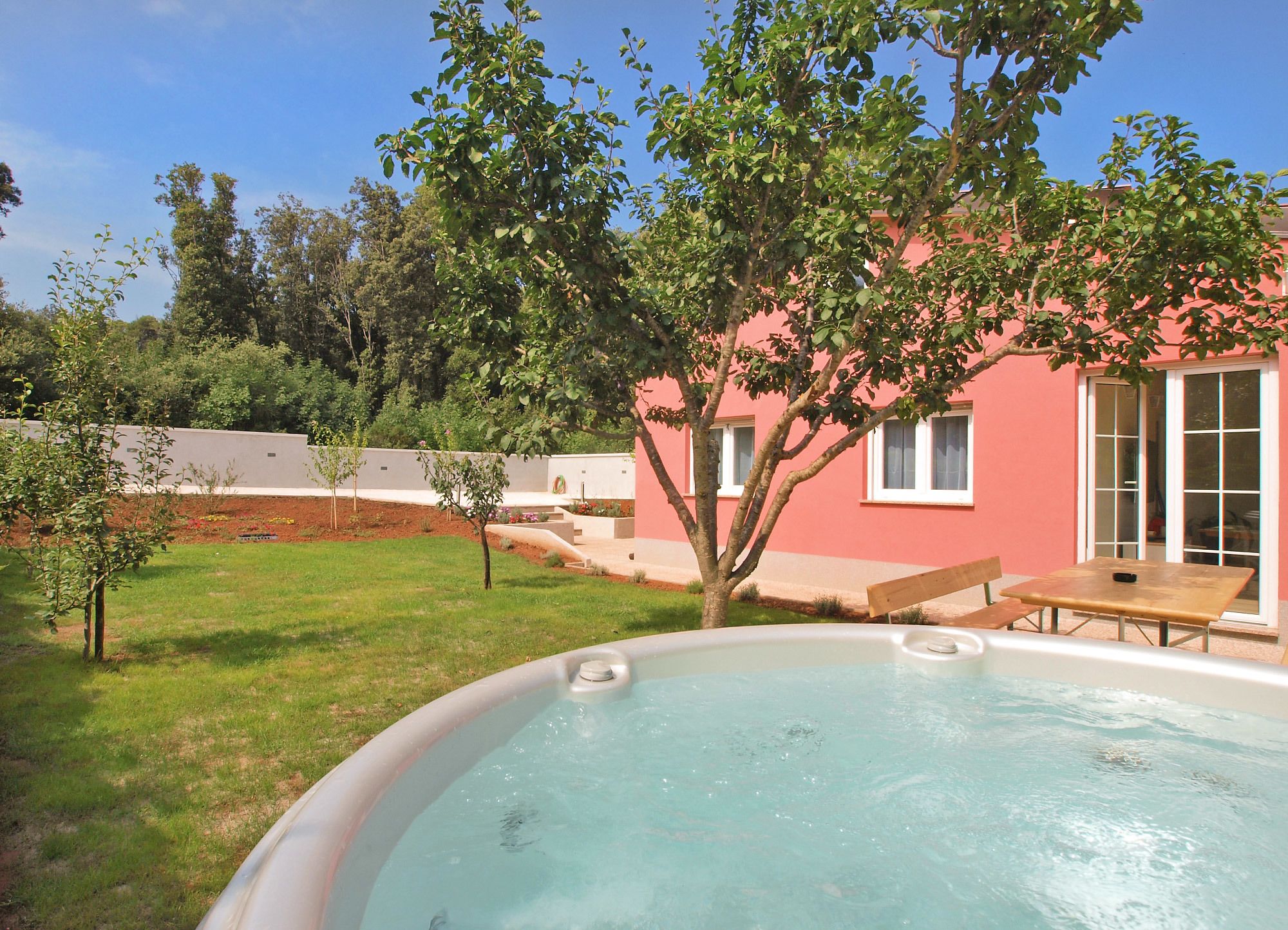 A hot tub in a backyard with a pink house, a tree, and a small patio table.