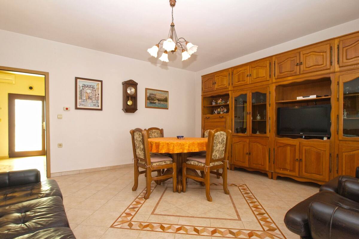 Una sala de estar con una mesa de comedor, sillas, un sofá, un televisor, armarios de madera y una alfombra estampada.