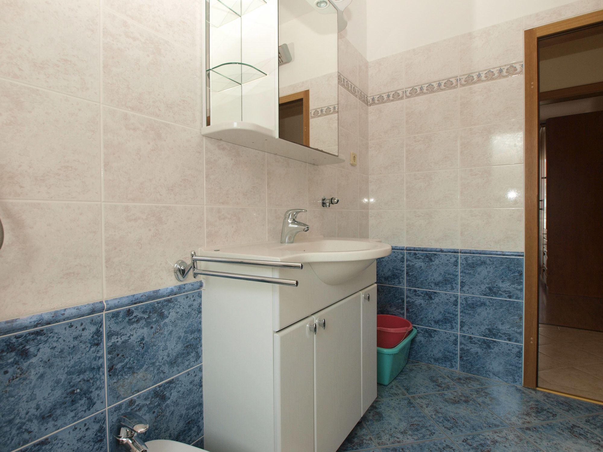 A bathroom with a white sink, a mirror, and blue-tiled walls.