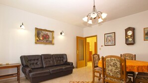 A living room with a dark brown leather sofa, a wooden dining table with floral chairs, a chandelier, and a clock on the wall. - Apartment 1704 (Medulin)