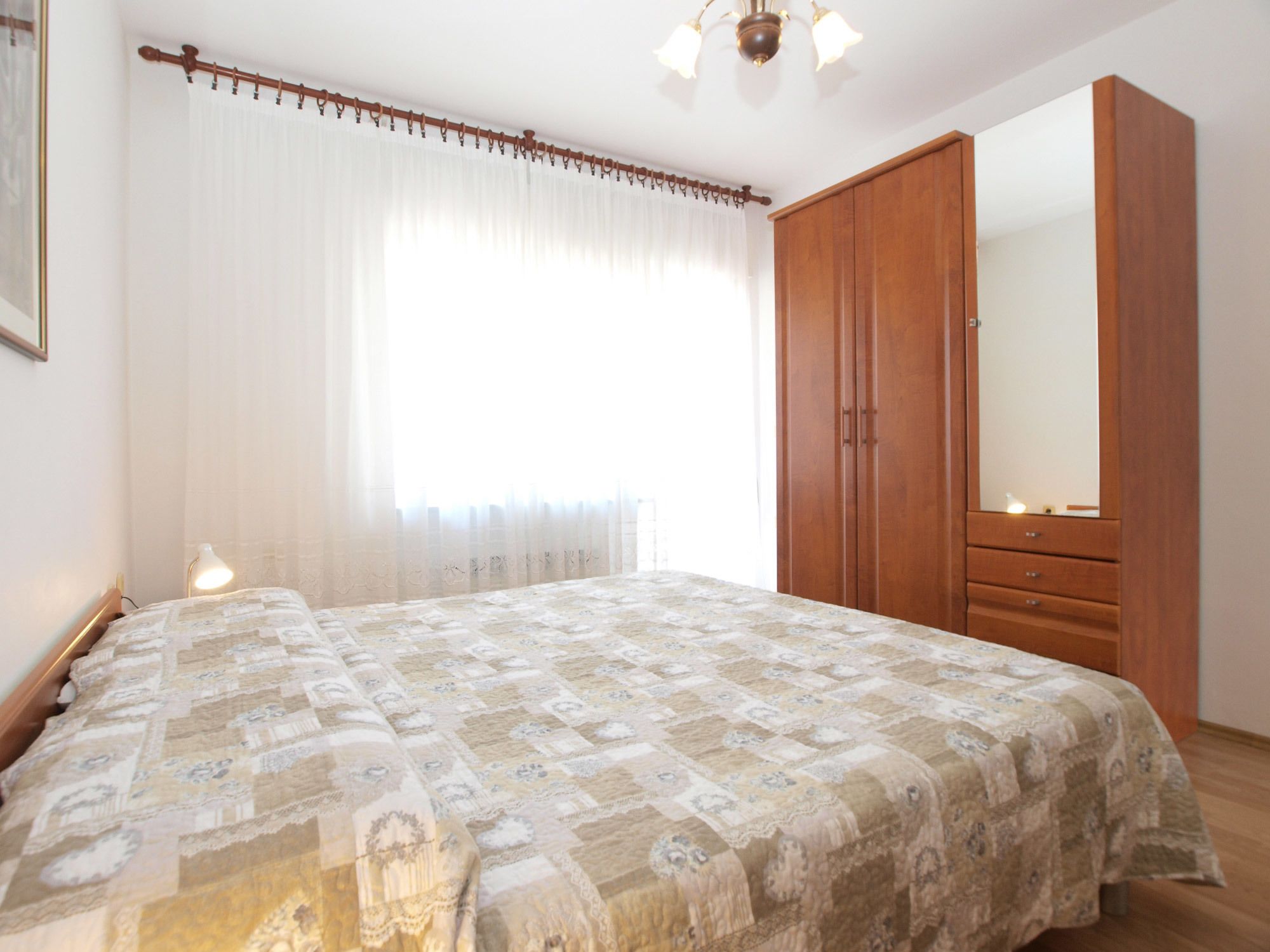 A bedroom with a bed, a wooden wardrobe, a mirror, and a window with curtains.