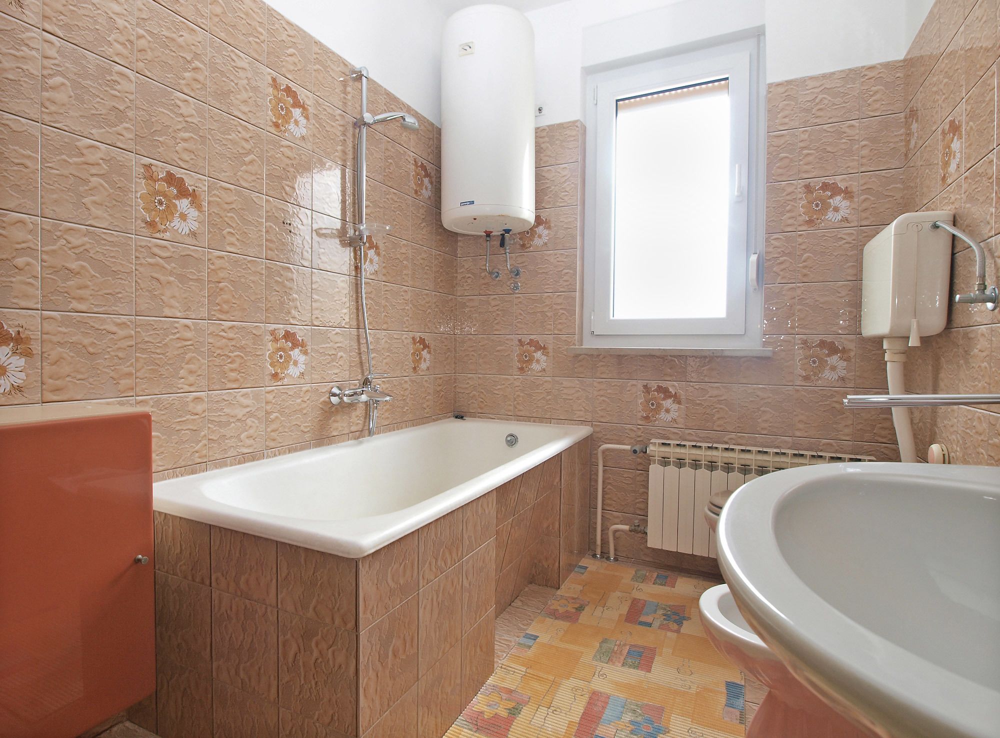 A bathroom with a bathtub, a toilet, a radiator, and a window.