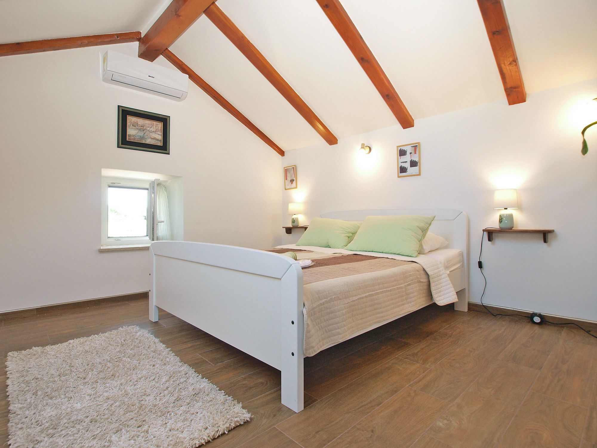 A bedroom with a bed, wooden beams, a window, and wall-mounted lights.