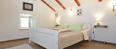 A bedroom with a bed, wooden beams, a window, and wall-mounted lights.