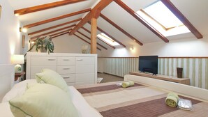 A high-ceilinged attic bedroom with exposed wooden beams, a large bed, a TV, and a view of the sky through skylights. - House 1708 (Barban)