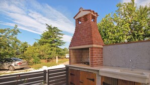 A brick barbecue grill with a chimney, a sink, and wooden cabinets. - House 1708 (Barban)