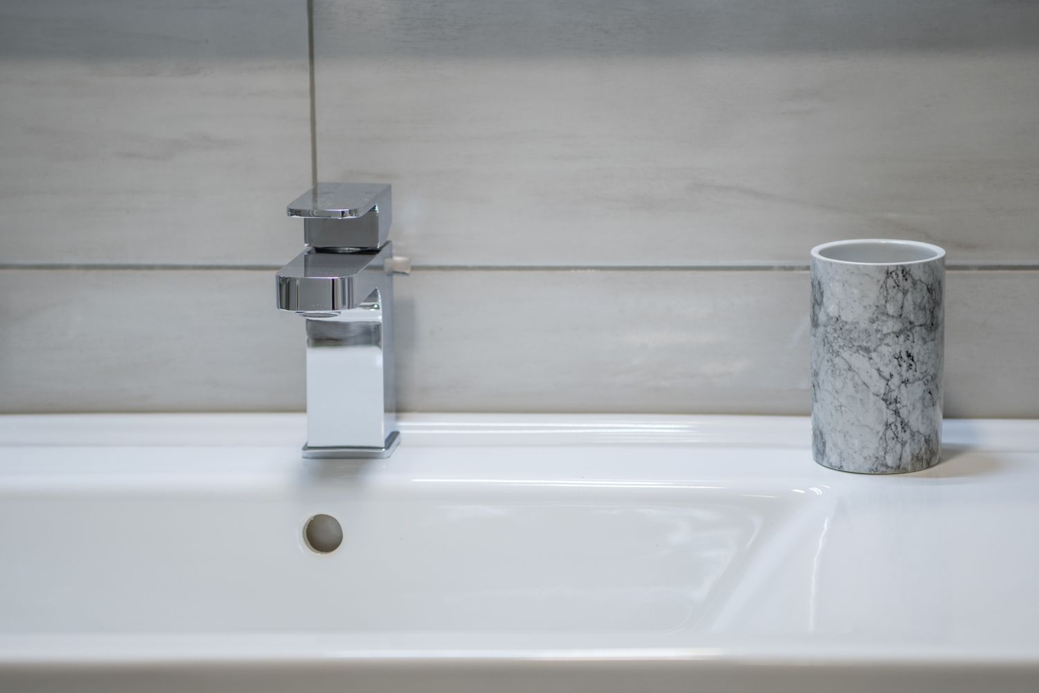 A bathroom sink with a chrome faucet and a marble mug on the counter.