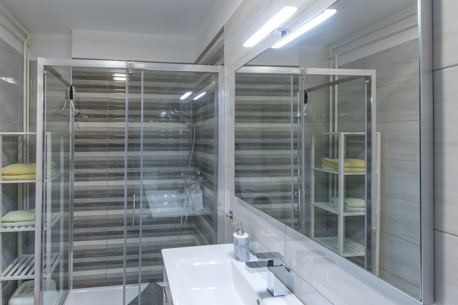Ein modernes Badezimmer mit einer Duschkabine aus Glas, einem weißen Waschbecken und Marmorarbeitsplatten.