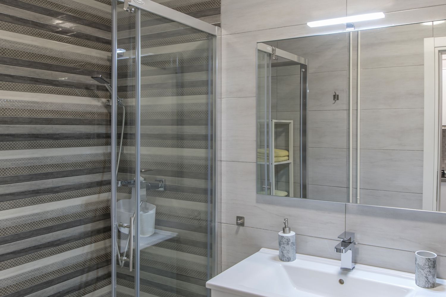 A modern bathroom with a glass shower enclosure, a large mirror, and a white sink with a marble-like countertop.