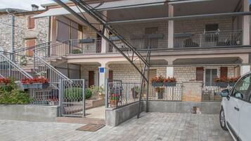 Un immeuble à plusieurs étages, avec un escalier menant à l’étage supérieur, des places assises à l’extérieur et une voiture garée devant.