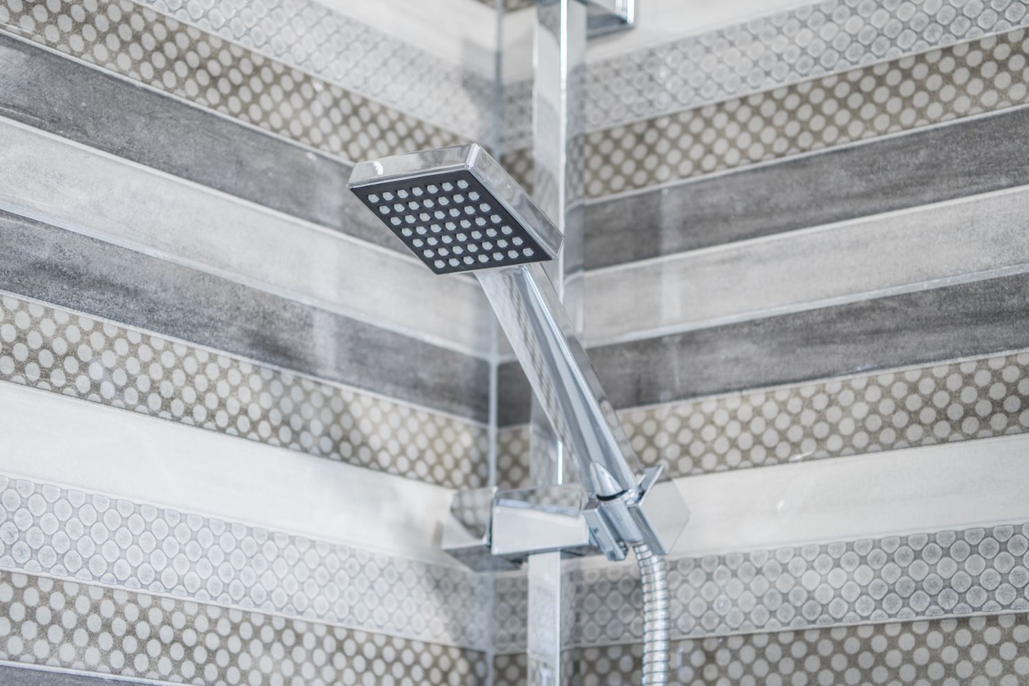 Eine Dusche mit einem eckigen Duschkopf und einem flexiblen Schlauch.