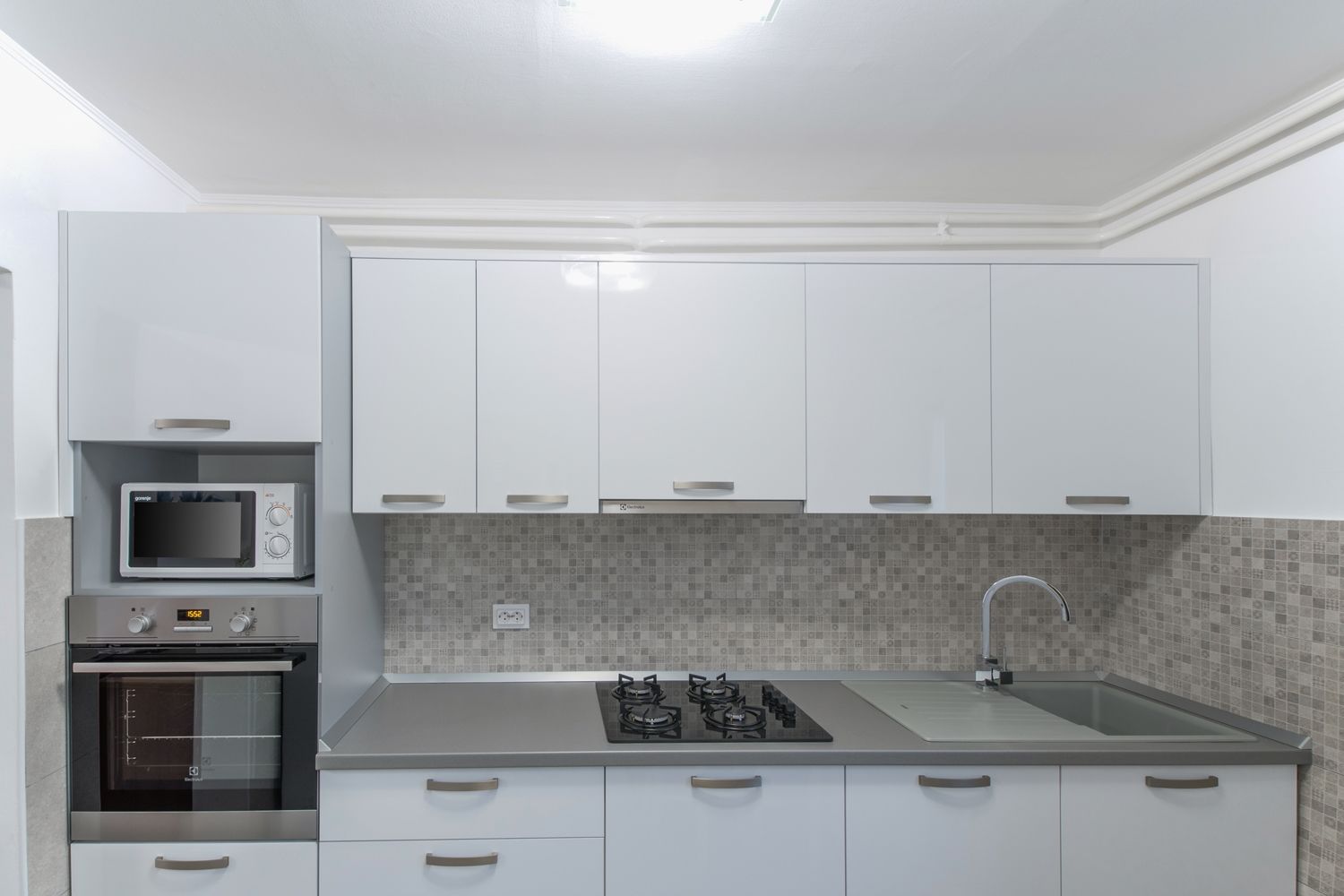 A modern kitchen with white cabinets, a microwave, an oven, a gas stove, and a sink.