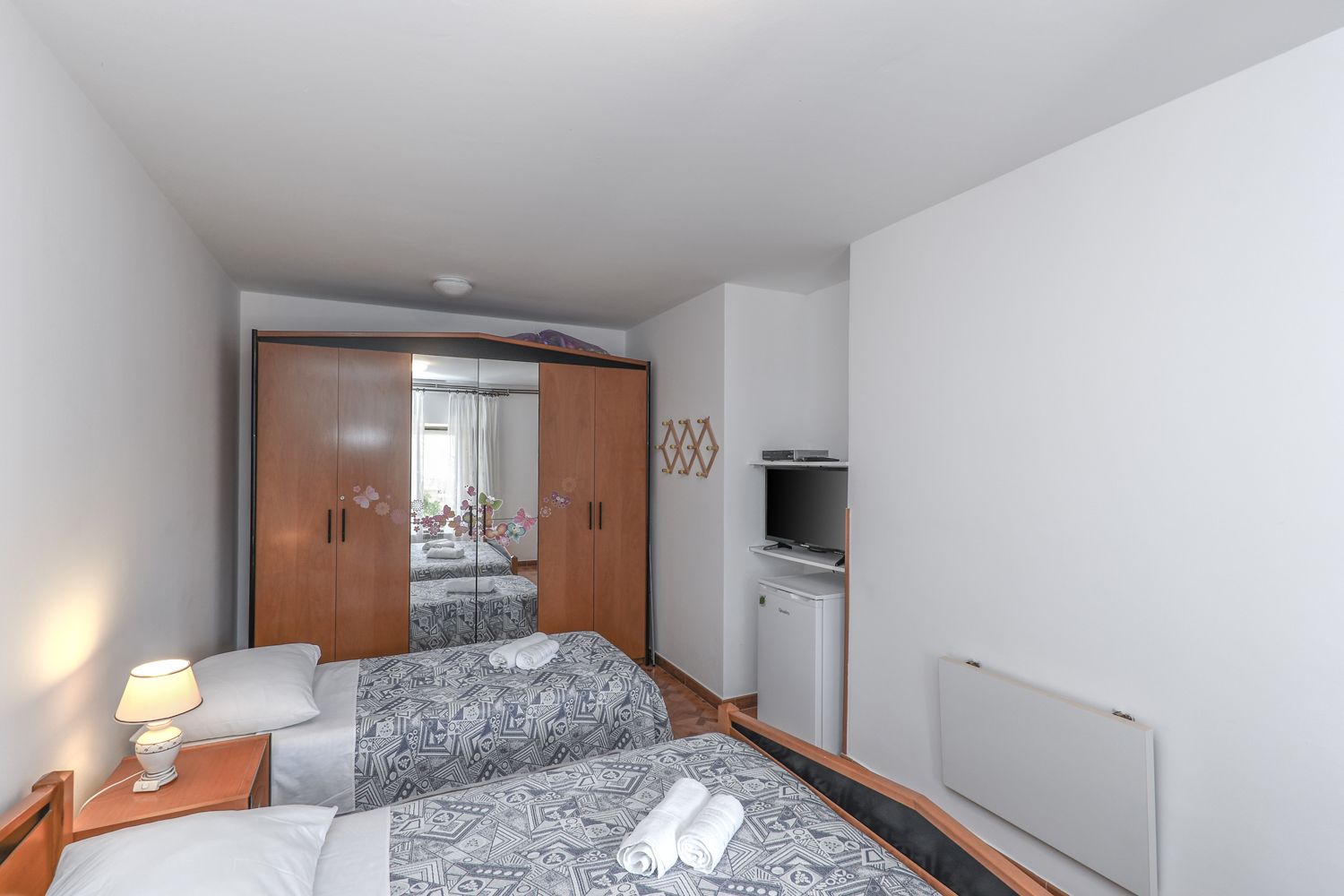 Habitación de hotel con dos camas, un armario, un televisor y un refrigerador pequeño.