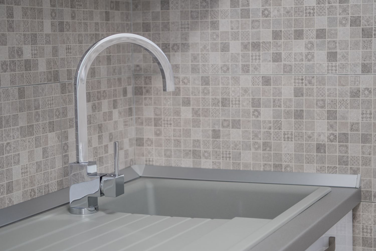 A modern kitchen with a stainless steel sink, a sleek faucet, and a tiled backsplash.