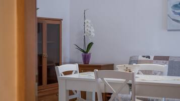 A dining area with a white table and chairs, a purple orchid plant, and a wooden cabinet.