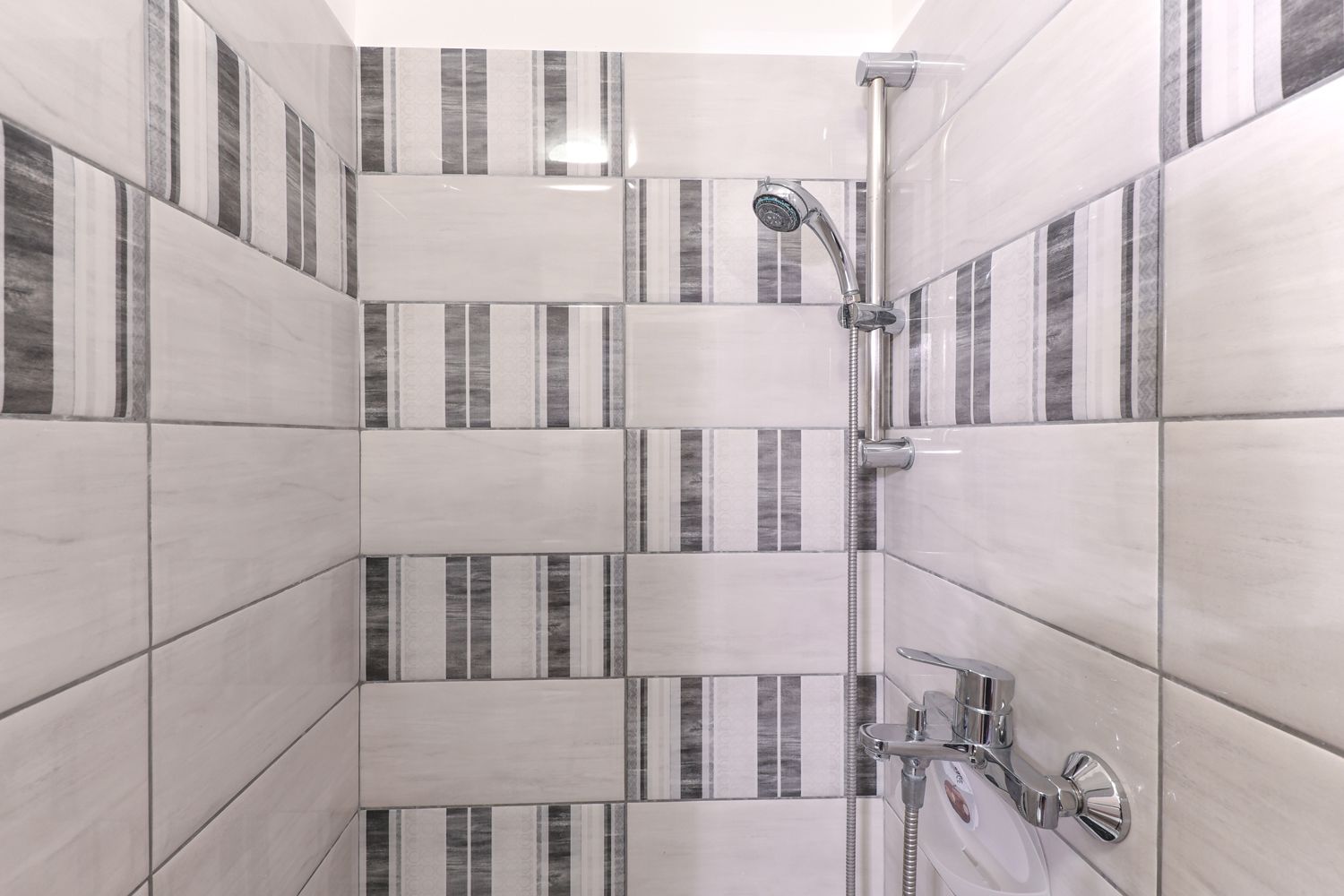 Une salle de bain moderne avec des murs recouverts de carreaux à rayures et une douche équipée d’un pommeau de douche amovible.