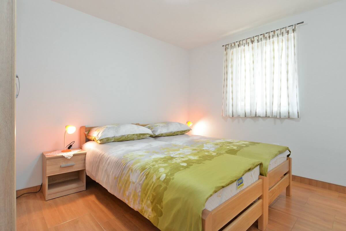 A bedroom with a bed, bedside table, lamp, and window with curtains.