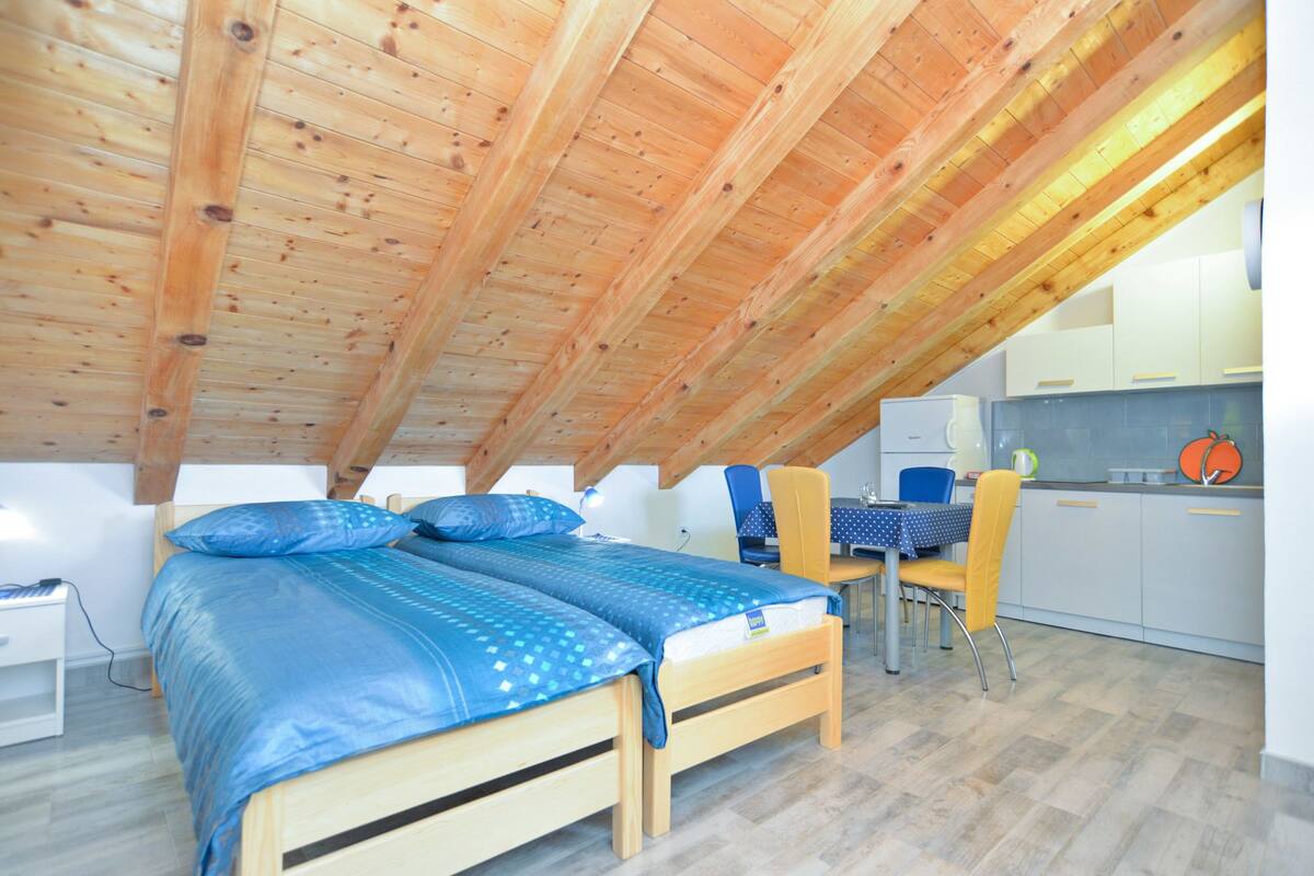 A cozy attic bedroom with two wooden beds, a small kitchenette, and a dining area.