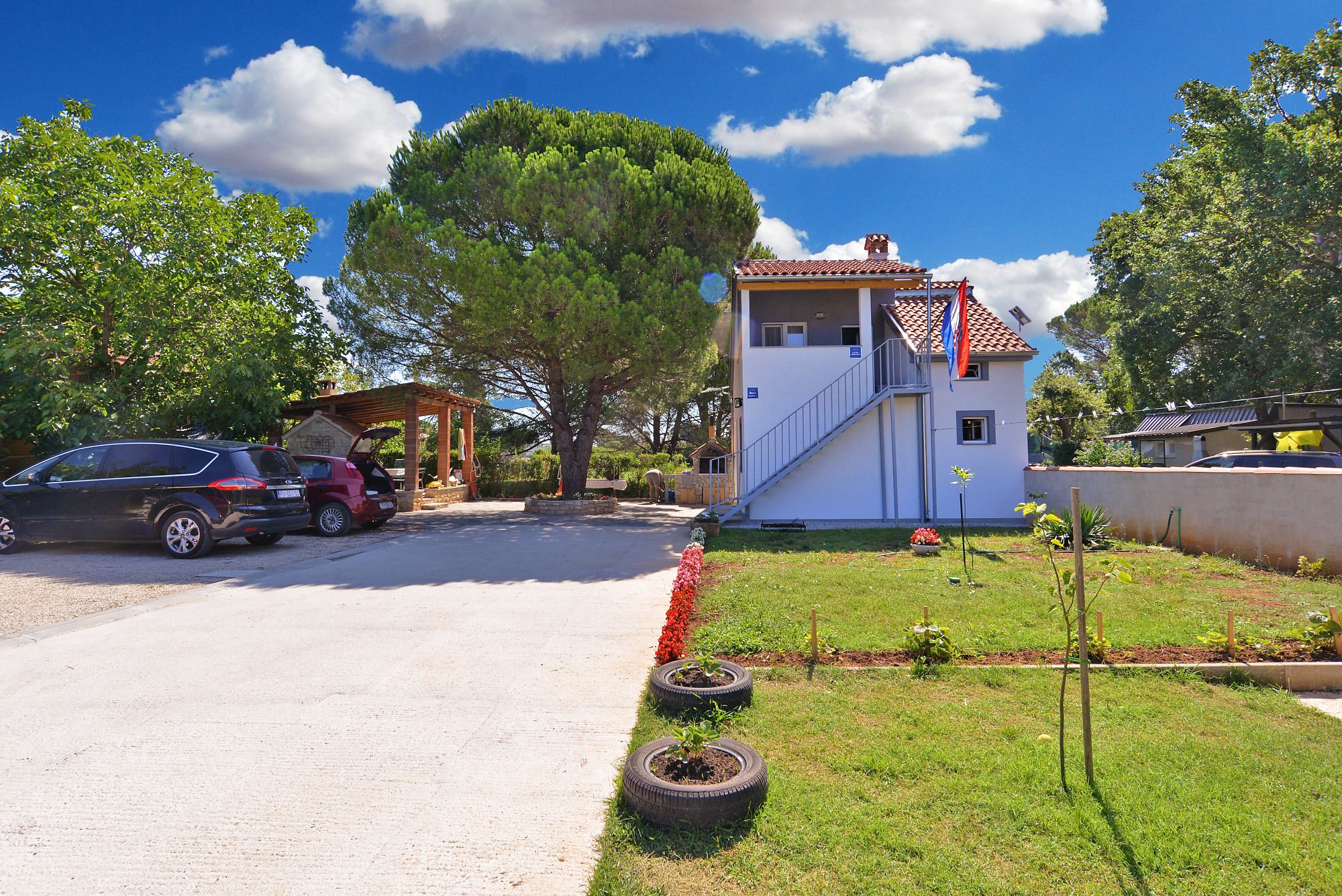 A two-story building with a red-tiled roof, a covered outdoor area, and a small garden with tire planters.