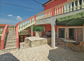 A patio area with a stone floor, a table with chairs, a fireplace, and a staircase with a railing. - House 1716 (Marcana)