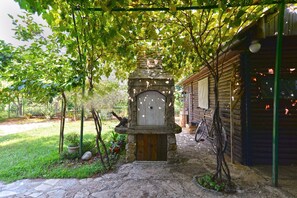 A stone archway leading to a wooden building with a door, surrounded by greenery and a bicycle. - Apartment 1725 (Vodnjan)