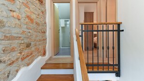 A staircase with a wooden handrail and black metal balusters, leading to a room with a white door and a brick wall. - House 1735 (Vodnjan)