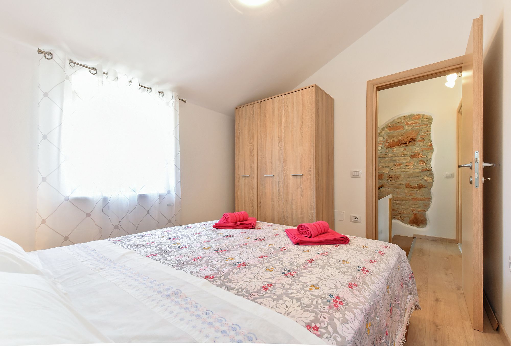 A bedroom with a bed, a wardrobe, and a door leading to a stone-walled room.