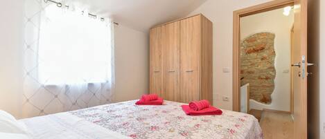 A bedroom with a bed, a wardrobe, and a door leading to a stone-walled room.