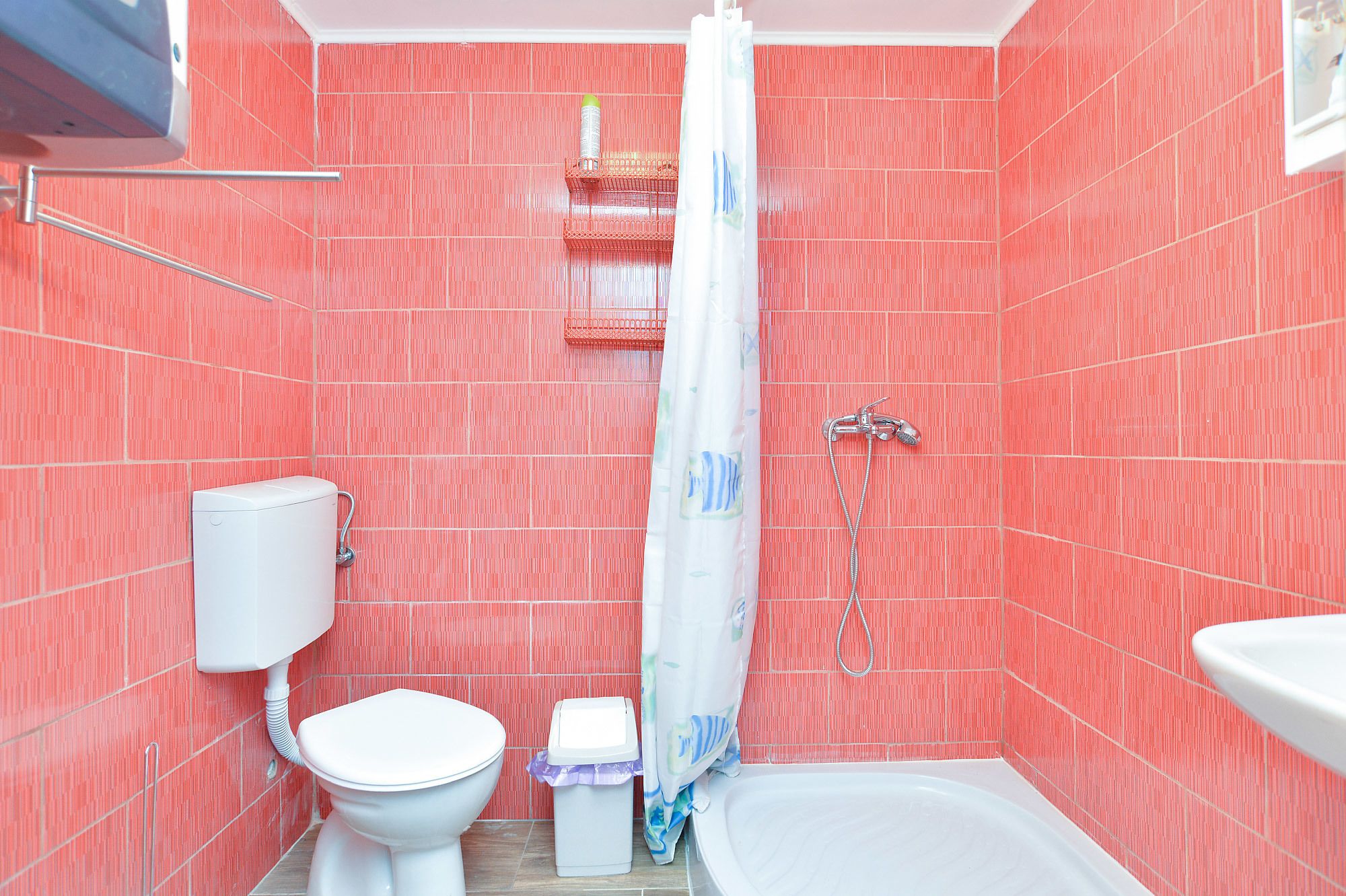 A bathroom with red tiled walls, a white toilet, a shower with a curtain, and a white sink.