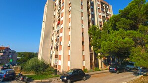 Un edificio residencial de varios pisos con balcones, una zona de estacionamiento con coches y vegetación circundante.