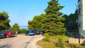 Un aparcamiento con varios coches, un gran pino y un edificio con antenas parabólicas.
