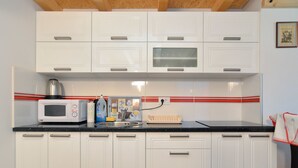A kitchen with white cabinets, a microwave, a kettle, and a red-striped backsplash. - Apartment 1739 (Medulin)