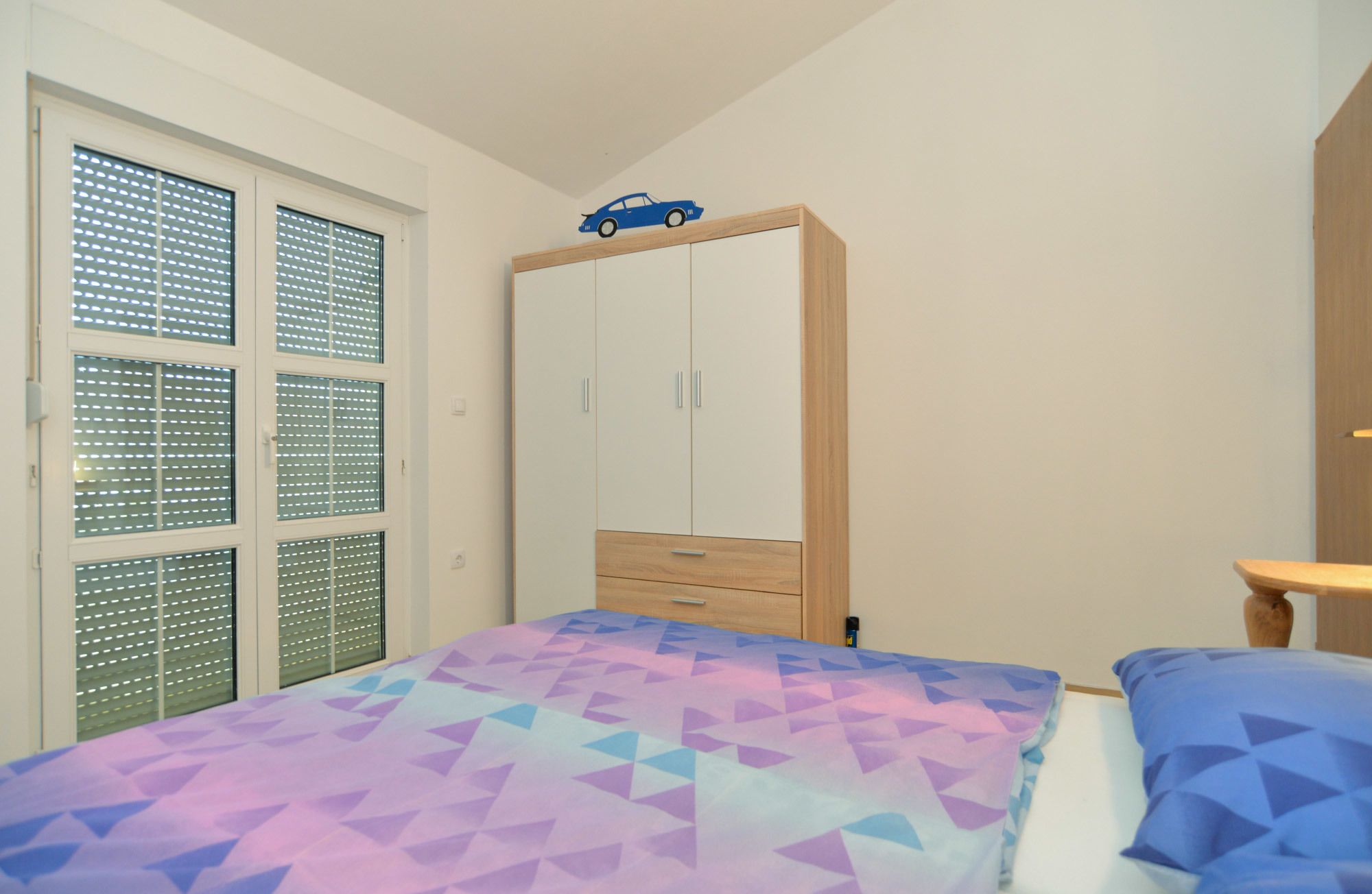 A bedroom with a bed, a wardrobe, and a window with blinds.