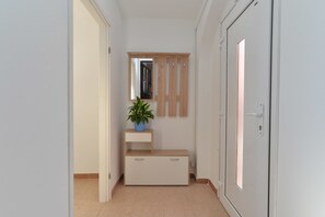 A hallway with a wooden bench, a potted plant, a mirror, and a door. - House 1753 (Fazana)