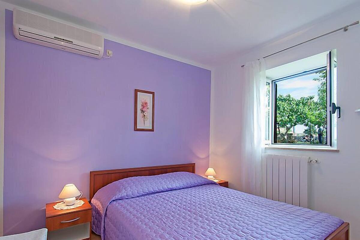 Une chambre avec un lit, deux tables de chevet avec des lampes, une fenêtre donnant sur un paysage verdoyant et un climatiseur fixé au mur.